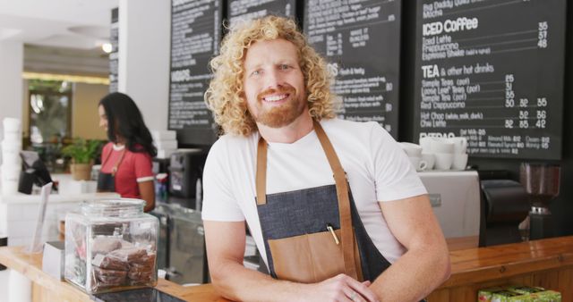 Portrait of happy caucasian male barista using tablet, smiling behind the counter in cafe. Local business owner and hospitality concept.