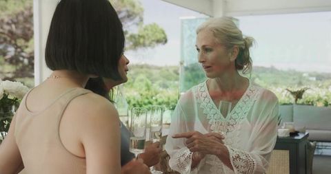 Multigenerational women chatting and toasting on sunlit patio with garden view, lace blouse