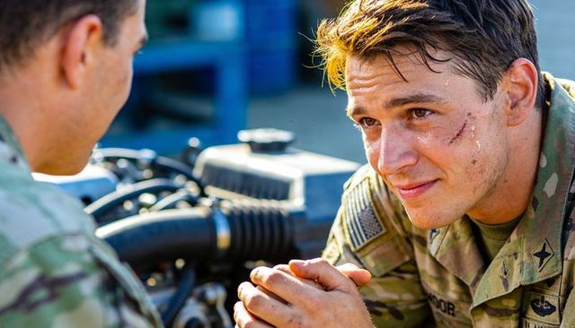 Young soldier leaning and clasping hands near vehicle engine during field maintenance