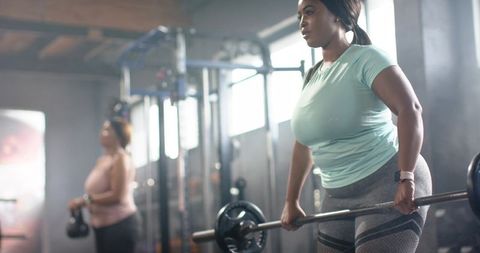Women lifting barbell and kettlebell during strength training in modern gym interior