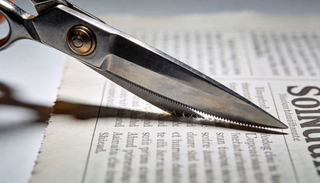 Vintage stainless steel scissors cutting newspaper serrated blade macro detail torn margin