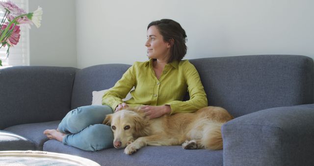 Caucasian woman smiling and sitting on couch with dog. domestic life, spending free time relaxing at home.