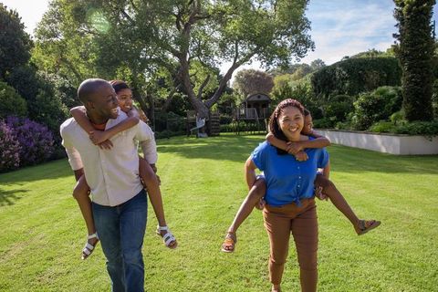 Diverse Family Carries Children Piggyback in Lush Backyard Setting