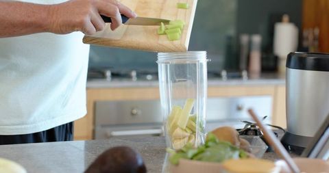 Preparing green smoothie: pouring chopped celery and banana into blender cup