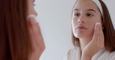 Woman Cleansing Face with Cotton Pad in Bathrobe