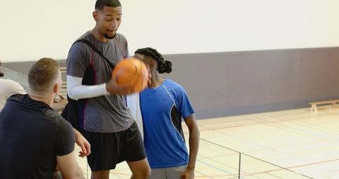 Young diverse men greeting teammate with basketball and duffel bag at indoor sports court