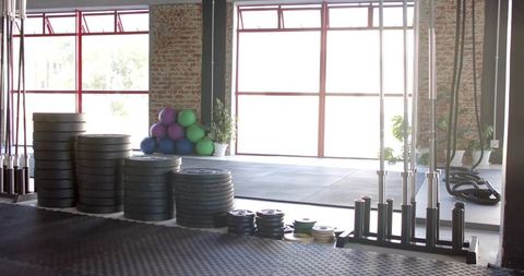 Stacking Bumper Plates and Barbells in Sunlit Industrial Gym with Large Windows