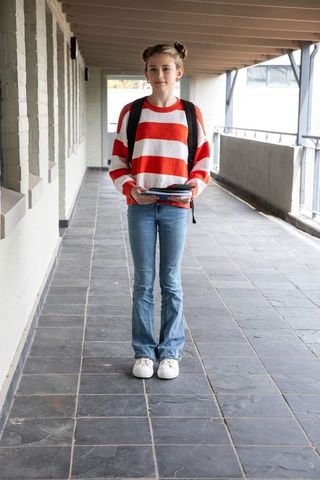 Teenage student holding notebooks in school corridor