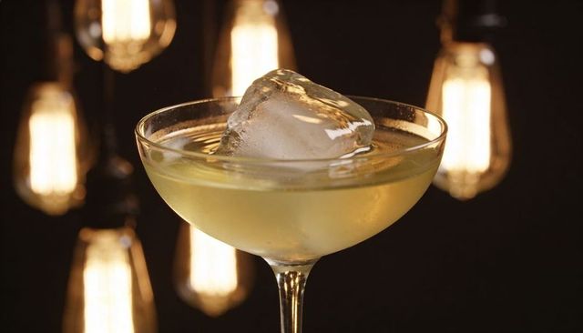 Coupe glass holding pale yellow cocktail with king cube under warm filament lights