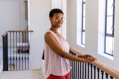 Confident african woman leaning on railing in bright modern home wearing sporty pink top