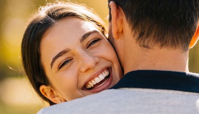 Young woman laughing while embracing partner during backlit golden-hour couple moment