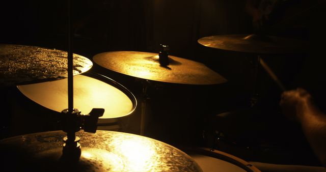 Medium close-up of drums and cymbals captured under warm lighting, highlighting percussion instruments. Ideal for music-related websites, advertisements for music gear, blogs about live performances, and educational materials on drumming techniques. Emphasizes ambiance and emphasis on musical focus.