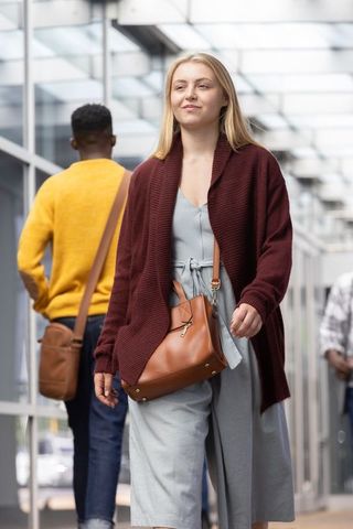 Young woman walking under glass canopy carrying tan leather bag, urban commuter lifestyle