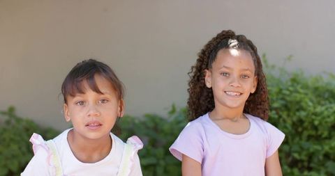 Smiling african american girls in pastel clothes standing outdoors backyard summer