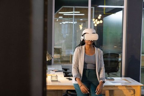 African American woman testing VR headset sitting on office desk in coworking workspace