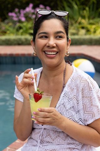 Smiling woman relaxing at backyard pool holding summer cocktail with strawberry garnish