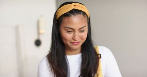 Asian woman smiling and looking down wearing yellow headband and casual white top