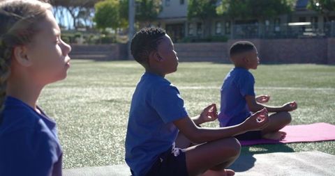 Teenage students practicing outdoor mindfulness and yoga on school field in blue shirts