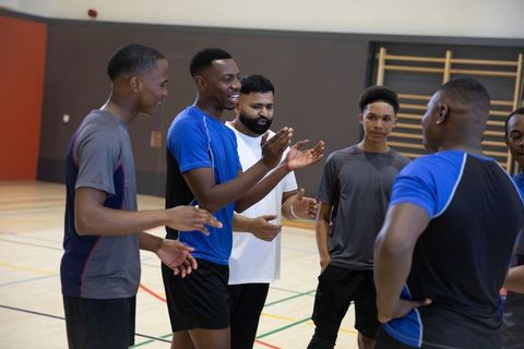 Youth sports team huddling while coach leading energetic discussion in school gym court