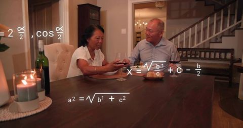 Mature couple clinking wine glasses at home dining table with equations overlay and candlelight
