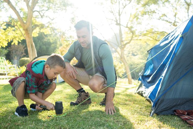 Father and son working together to set up a tent at a campsite. Ideal for use in content related to family bonding, outdoor activities, camping trips, and nature adventures. Perfect for promoting camping gear, family vacations, and outdoor lifestyle.