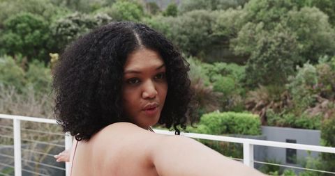 African American Woman Looking Over Shoulder Stretching Arm on Balcony Overlooking Greenery