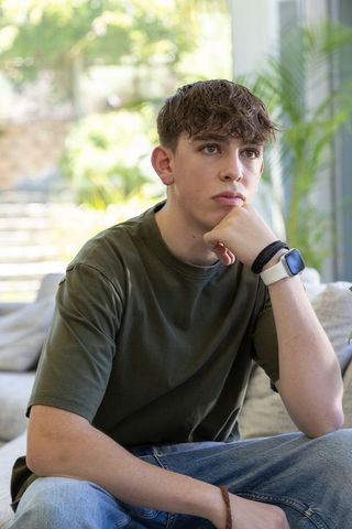 Thoughtful teen sitting on sofa wearing smartwatch and olive t-shirt in bright modern living room