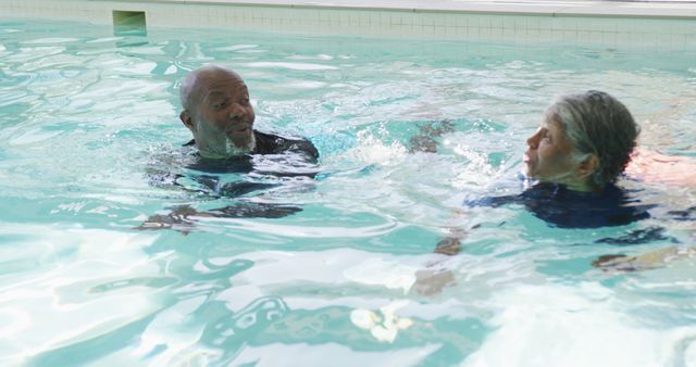 Two senior African Americans are seen swimming in an indoor pool. They appear to be engaging in a regular fitness routine. This image can be used for promoting active lifestyles, fitness programs for the elderly, and wellness activities for seniors. It highlights health, well-being, and the importance of staying active in older age.