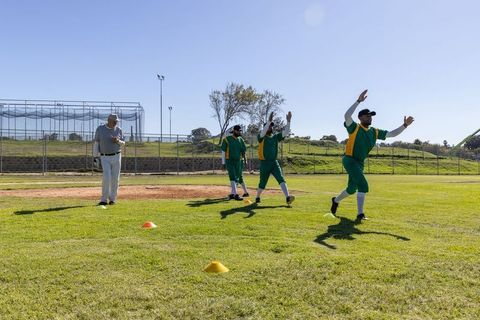 Male baseball team practicing field drill on sunny ballpark with coach supervising