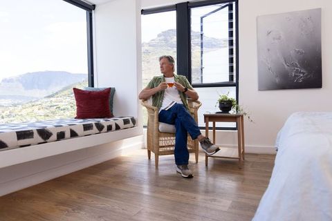 Mature man relaxing in rattan chair with mountain view in sunlit minimalist bedroom