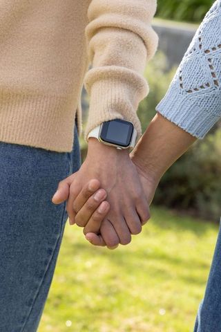 Couple holding hands wearing smartwatch in park, knit sweaters and wrist close-up