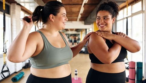 Smiling plus-size women stretching and encouraging each other in bright fitness studio