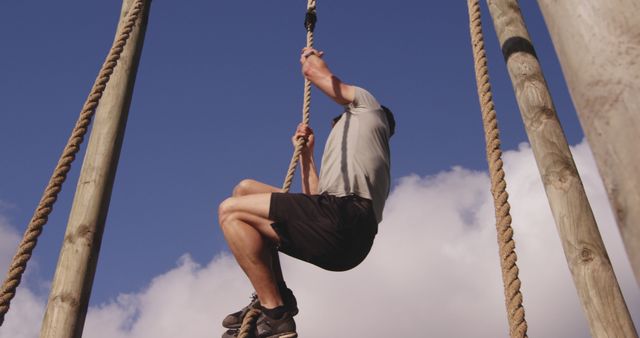 Man showing determination while climbing rope in outdoor gym. Perfect for fitness and sports promotions, motivational posters, strength training programs, and outdoor activity advertisements.