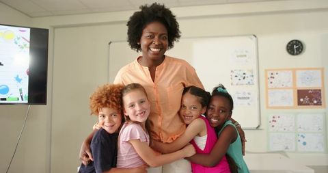 African teacher hugging diverse elementary students in classroom expressing warmth and teamwork