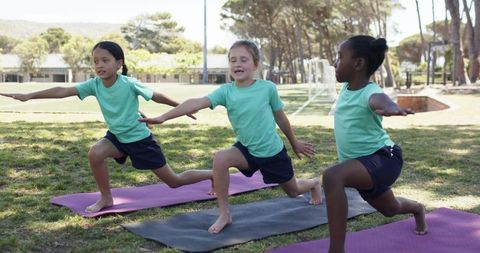 Multicultural schoolgirls practicing yoga lunge stretches on sunlit school sports field