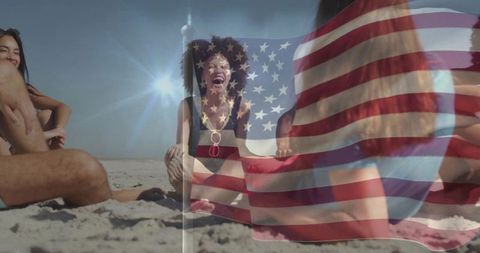 Laughing woman holding American flag fabric on sunlit beach with friends, summer celebration
