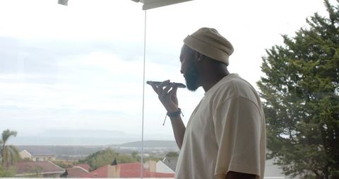 Man standing on balcony speaking into smartphone with coastal rooftops and overcast sky