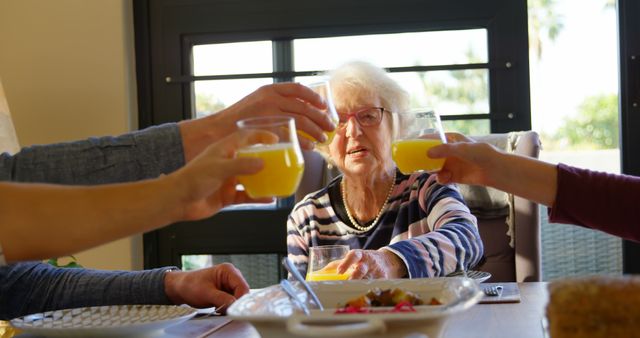 Senior woman enjoying family breakfast while toasting with orange juice, creating happy and bonding moments over a shared meal. Suitable for promoting family values, senior care, or advertising breakfast foods.