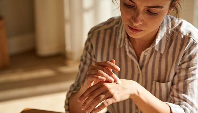Woman applying hand cream in sunlit room wearing striped shirt natural self-care moment