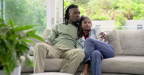 Cuddling Diverse Couple Relaxing on Cozy Modern Gray Sofa by Glass Doors Overlooking Garden