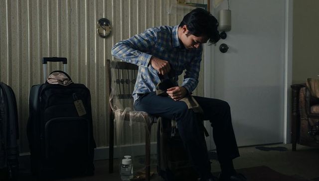 Traveler polishing shoe in dim motel room with two suitcases late night