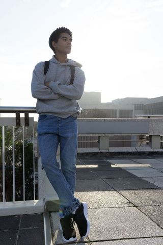Late-teen standing on rooftop leaning on railing wearing hoodie and backpack