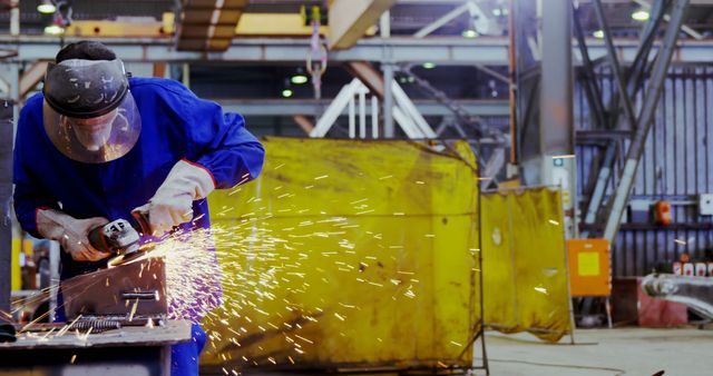 Worker in protective gear using a tool in a factory, generating bright sparks. Useful for industrial, manufacturing, or engineering contexts, safety gear promotion, or educational materials on factory work environments.