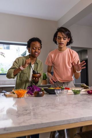 African american woman and asian man preparing fresh vegetable bowls on marble island