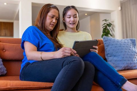 Asian mother and daughter bonding while using tablet on sofa
