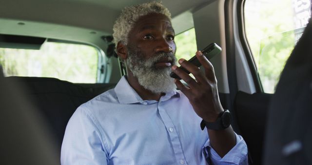 Senior businessman engaging in a conversation on a walkie-talkie while sitting inside a car. Useful for concepts related to mobile work settings, communication technology, professional activities, and dynamic business environments.