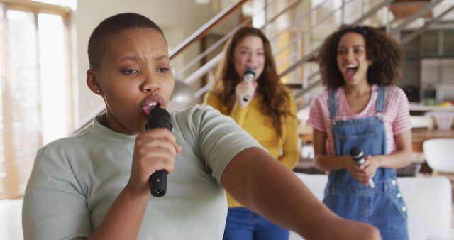 Three young adults are having fun singing karaoke at home. The main subject is passionately singing into the microphone while the two friends cheer and enjoy in the background. Perfect for illustrating themes of friendship, leisure activities, music, and indoor fun. Can be used in publications or blogs about social interactions, home entertainment, and youth culture.