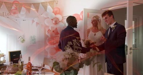 Groom and bride greeting guest at decorated reception doorway with balloons and bouquet
