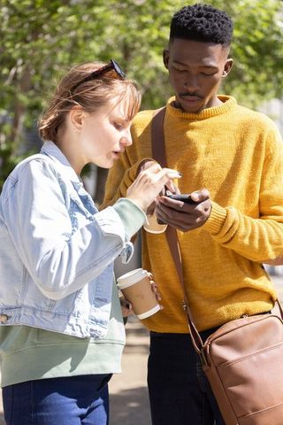 Young multicultural friends checking smartphone together on sunlit city sidewalk
