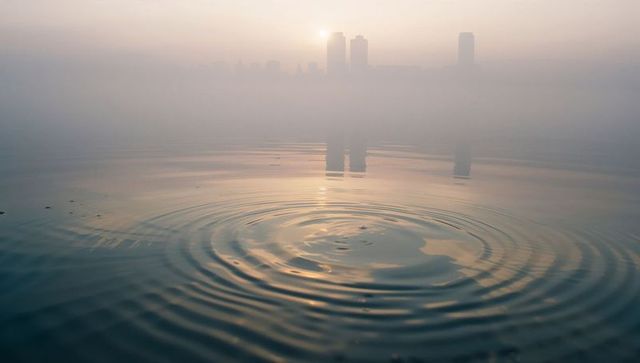 Rippled water reflecting misty city sunrise skyline silhouette